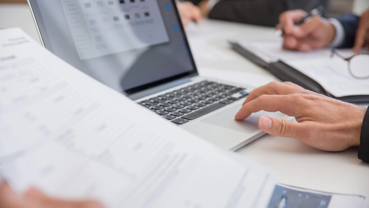 Pessoa trabalha com documentos e notebook.